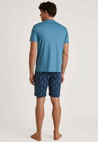 Lichtblauw shirt met korte mouwen, gecombineerd met patroonbroek in marineblauw met een bloemenmotief. Het materiaal lijkt lichtgewicht en casual te zijn.