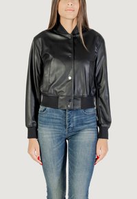 Giubbotto di pelle nero corto con una texture liscia, chiusura a bottoni e polsini a costine, abbinato a jeans blu.