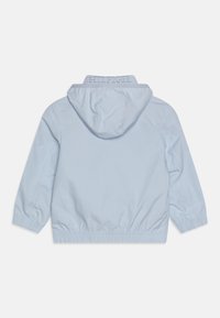 Světle modrá mikina s kapucí, elastickými manžetami a lemem. Má vyšívané logo na límci, hladký materiál a volný střih.