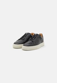Czarne skórzane sneakersy z perforowanym detalem na palcach, czarne sznurowadła i biała gumowa podeszwa. Wnętrze wykończone jest brązową podszewką.