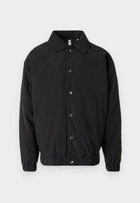 Melnā jakā ar apkakles izgriezumu, sprādziņu priekšpusi, elastīgām piedurknēm un sānu kabatām. Gluda auduma vienkāršs dizains.