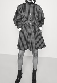 Svart och vit rutigt klänning med hög krage, elastisk midja, långa ärmar och sidofickor, kombinerad med svarta ankelstövlar.