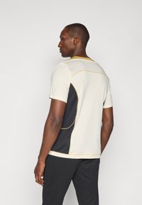 Camiseta atlética de manga corta en gris claro con paneles negros, costuras amarillas y una textura de malla, con cuello redondo y acentos en contraste.