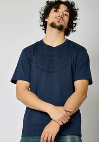 T-shirt bleu marine à manches courtes en coton avec un imprimé logo texturé au centre. Couper pour une coupe décontractée, il possède un col rond.