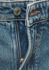 Blugi din denim cu închidere cu buton metalic, cusături contrastante portocalii și un fermoar vizibil. Prezintă o culoare albastră estompată și o textură netedă.