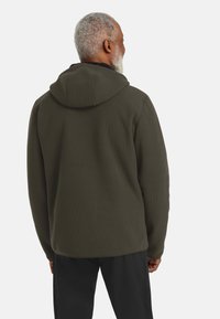 Diepgroene geribde hoodie met een grote capuchon, gemaakt van een gestructureerde stof. De achterkant heeft een relaxed fit en lange mouwen.