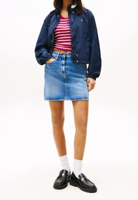 Marinblå vindjacka, röd och vit randig crop top, jeanskjol, svarta loafers, vita strumpor. Detaljer inkluderar knappar och midjeband.