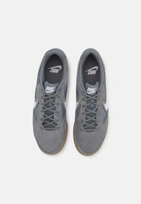 Sive Nike superge iz sukna in mrežnega materiala, s belim logotipom, teksturirano površino in gumijastim podplatom. Oblikovane za udobje in podporo.