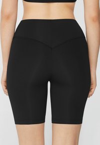 Pantalones cortos de ciclismo negros de cintura alta con una textura suave y elástica. Detalles de costura en la parte trasera, ajustados hasta la mitad del muslo. Sin logotipos visibles.