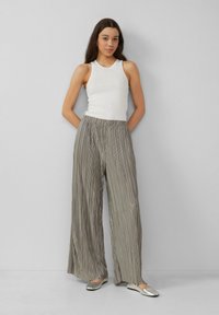 Witte mouwloze tanktop met versieringen, gecombineerd met hooggewaist, grijsgemaakte plooibroek met brede pijpen en zilveren platte schoenen.