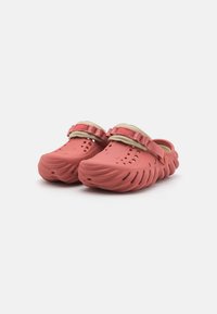 Clogs in coral pink, made of lightweight material. Features ventilation holes, a textured sole, and a removable strap.