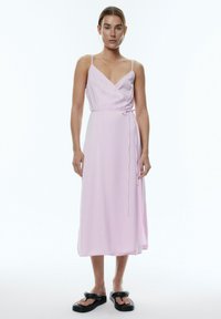 Wickelkleid in Hellrosa, mit dünnen Trägern, einem V-Ausschnitt, einem gebundenen Gürtel in der Taille und einer fließenden, knielangen Silhouette.