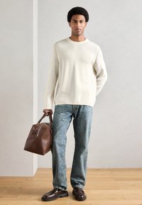 Krēmkrāsas džemperis, gaiši zili džinsi, brūna ādas soma un tumši apavi. Džempera gluda tekstūra, strukturēta soma ar rāvējslēdzēja akcentu.