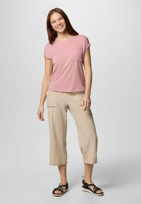 T-shirt rosa chiaro a maniche corte con taschino sul petto, abbinato a pantaloni cropped beige e sandali neri con cinturini. Tessuto morbido, design casual.