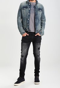 Džínová bunda v světle modré, šedé tričko s potiskem, černé seprané džíny a tmavé tenisky s bílou podrážkou.