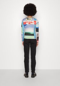 Maglietta a maniche lunghe con grafiche e vari motivi colorati, abbinata a pantaloni neri slim-fit e scarpe nere. Tessuto morbido ed elastico.