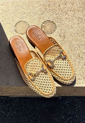 Chaussures à enfiler tressées beiges avec des accents en cuir et des éléments en métal, présentant une texture semblable à celle d'un panier et un design à orteil arrondi.