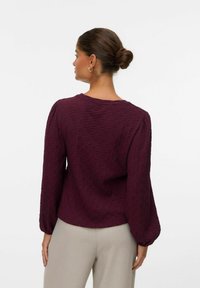 Mauve textuur blouse met geplooide lange mouwen en een ronde halslijn, van achteraf gezien, gecombineerd met lichtgekleurde broeken.