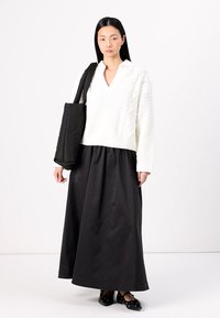 White knitted sweater with a textured pattern and V-neck, paired with a long black skirt and flat black shoes, carrying a black tote bag.