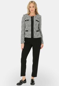 Szara i czarna marynarka o fakturze, o dopasowanym kroju, z czarnym obszyciem i dwoma przednimi kieszeniami; zestawiona z czarnymi prostymi spodniami i błyszczącymi mokasynami.