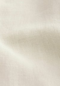 Gestructureerde crèmekleurige stof met een subtiele weving. Zachte, gladde oppervlakte; lichtgewicht en luchtig uiterlijk, geschikt voor verschillende textieltoepassingen.