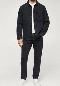 Chaqueta de mezclilla negra con dos bolsillos en el pecho, combinada con pantalones de mezclilla negros a juego. Camiseta blanca debajo; zapatillas blancas completan el conjunto.