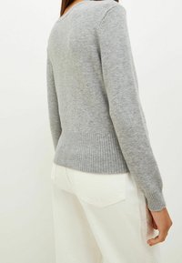 Pull gris en tricot avec un ourlet et des poignets côtelés, doté d'un col rond et d'une texture douce, associé à un pantalon blanc à jambes larges.