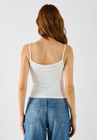 Hvid tætsiddende tanktop med tynde stropper, lavet af et glat stof, der er sat sammen med højtaljede blå denimbukser. Minimalistisk design og blød tekstur.