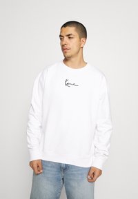 Witte sweatshirt met een ronde hals en lange mouwen, voorzien van een zwart handgeschreven logo op de borst. Draag het met lichtblauwe jeans.