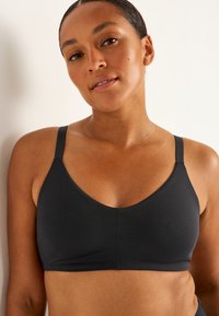 Svart bralette med en slät textur, V-ringad design, justerbara band och minimala sömdetaljer, som erbjuder en enkel och funktionell stil.