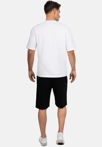 Wit katoenen T-shirt met korte mouwen, ronde hals en een ontspannen pasvorm, gecombineerd met zwarte shorts. De schoenen zijn wit met subtiele accenten.