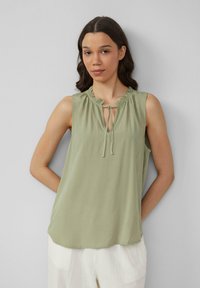 Blouse sans manches vert clair avec un col froncé et un détail à nouer, fabriquée dans un matériau lisse. Présente une coupe décontractée et un léger éclat.