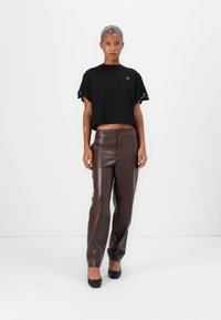 Black cropped t-shirt with lace trim on sleeves; brown leather pants with a button closure; model wears black high-heeled shoes.
