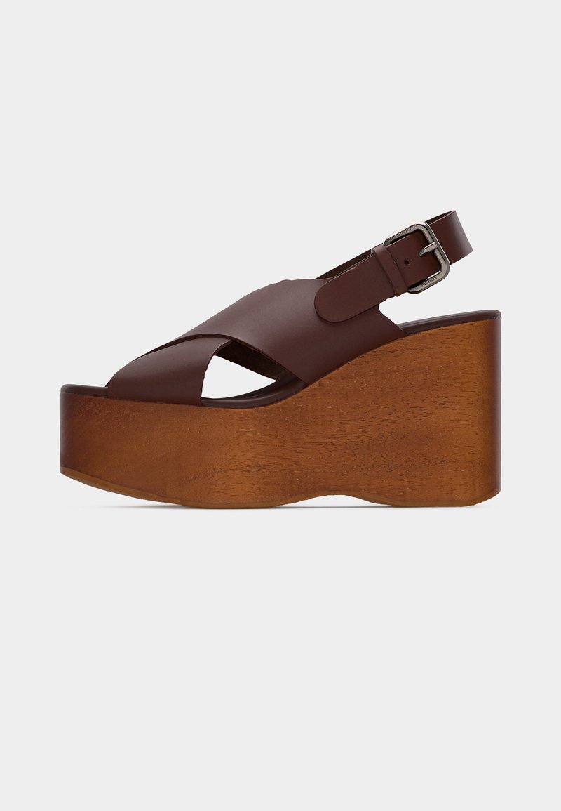 Sandale plateforme en cuir marron avec talon compensé en bois, brides croisées et boucle argentée réglable sur la bride de cheville.