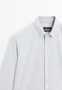 Koszula na guziki w jasnoniebieskie i białe paski. Wykonana z miękkiego materiału, z klasycznym kołnierzem i białymi guzikami. Posiada pionowe paski.