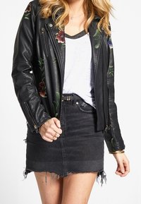 Czarna skórzana kurtka motocyklowa z kwiatowym haftem, zestawiona z przetartą czarną spódnicą dżinsową, z postrzępionym dołem i klasycznymi detalami w postaci zamków.