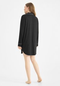 Camisa de dormir negra de manga larga con ribete blanco, dobladillo curvado y tejido suave, con aberturas laterales para mayor comodidad.