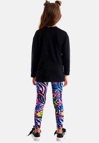 Zwarte longsleeve top, kleurrijke legging met patronen in roze, blauw en groen, en zwarte sneakers met strikjes op de hak.