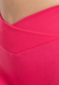 Fuchsiový sportovní pas s žebrovanou strukturou, s plochými švy. Hladký materiál klesá dolů bez dalších detailů.