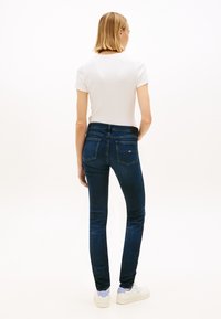 Jeans de ganga escura e fina com cintura média e bolsos traseiros, combinados com uma t-shirt branca justa e tênis brancos.