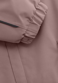 Rosa vattentät jacka med elastiska ärmslut och knappdetalj, slät struktur, med kontrasterande mörka sömmar längs sömmen.