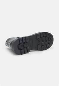 Bota de goma negra con suela texturizada, que cuenta con profundas ranuras para tracción, puntera reforzada y una sección superior lisa.