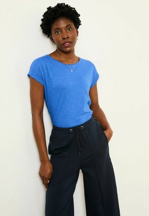 Blaues kurzärmeliges T-Shirt aus leichtem Stoff, kombiniert mit locker sitzenden schwarzen Hosen mit Kordelzug und Seitentaschen.