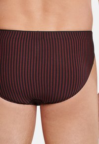 Slip da bagno da uomo neri con righe verticali rosse. Presenta un materiale liscio e elastico e un design della vita pulito.