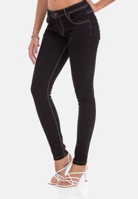 Zwarte skinny jeans met gouden stiksel, vijf zakken en een slank ontwerp. Gecombineerd met witte sandalen met bandjes.