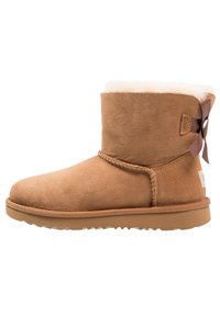 Korte brune semskede ankelstøvler med rund tå, fluffy kremfôr og en liten brun bue pyntet på siden. Gummisåle.