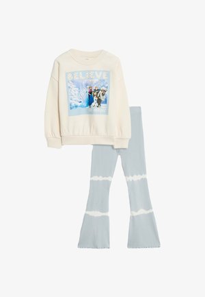 Cremefarbener Sweatshirt mit einem grafischen Druck, der Figuren und Text zeigt. Ausgestellte hellblaue Leggings mit einem Batikmuster.