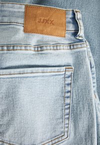 Ljusblå denimjeans bakvy med brun lädermärke som har texten "JUXX" och synliga sömnadsdetaljer.