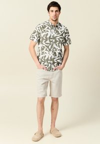 Korte mouwen shirt in groen en wit abstract patroon, gecombineerd met beige shorts. Lichtgewicht stof, knoopsluiting aan de voorkant, ontspannen pasvorm, casual schoeisel.