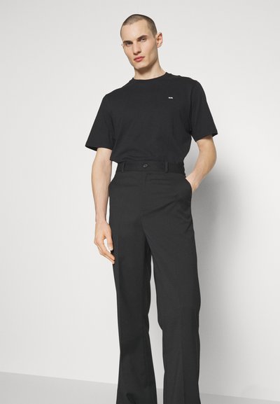 Black cotton t-shirt with short sleeves and a small logo, paired with black trousers featuring a belt and button closure, smooth texture.